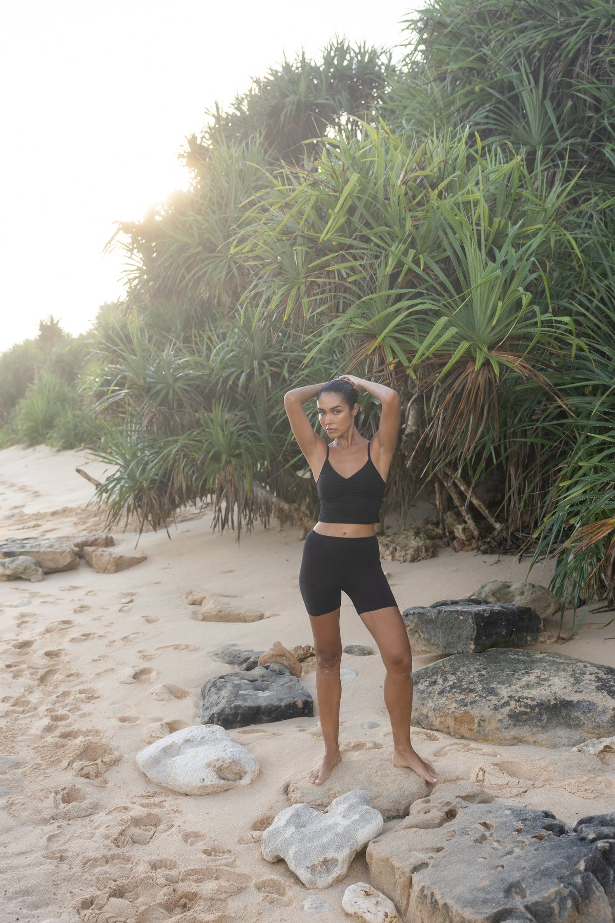 Two women on a rocky beach, one wearing an Adjustable Cotton Cami and matching shorts in Black Mist, the other in a white tank and black shorts #Color_Black Mist