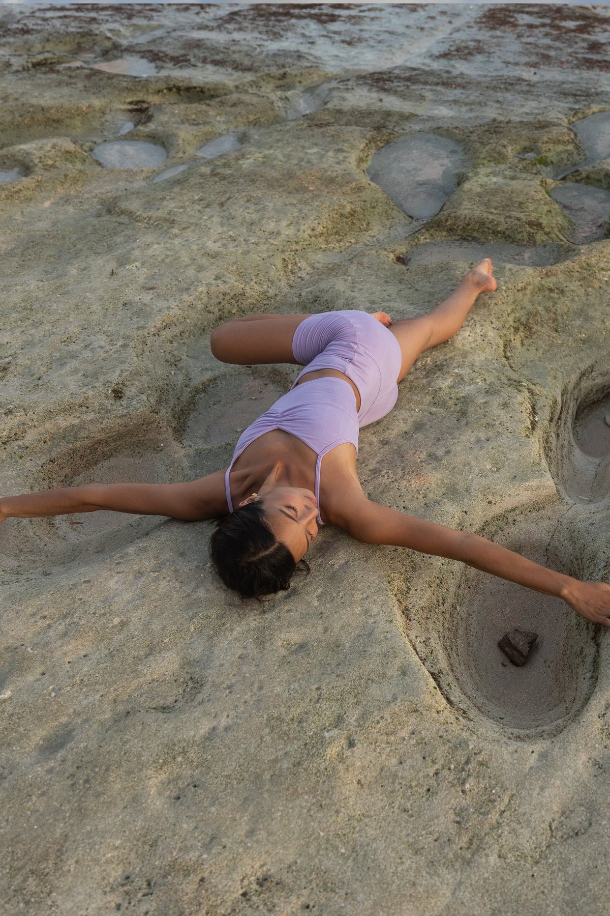 Woman lying on beach rocks in a star pose wearing an Adjustable Cotton Cami and matching shorts in Lilac #Color_Lilac