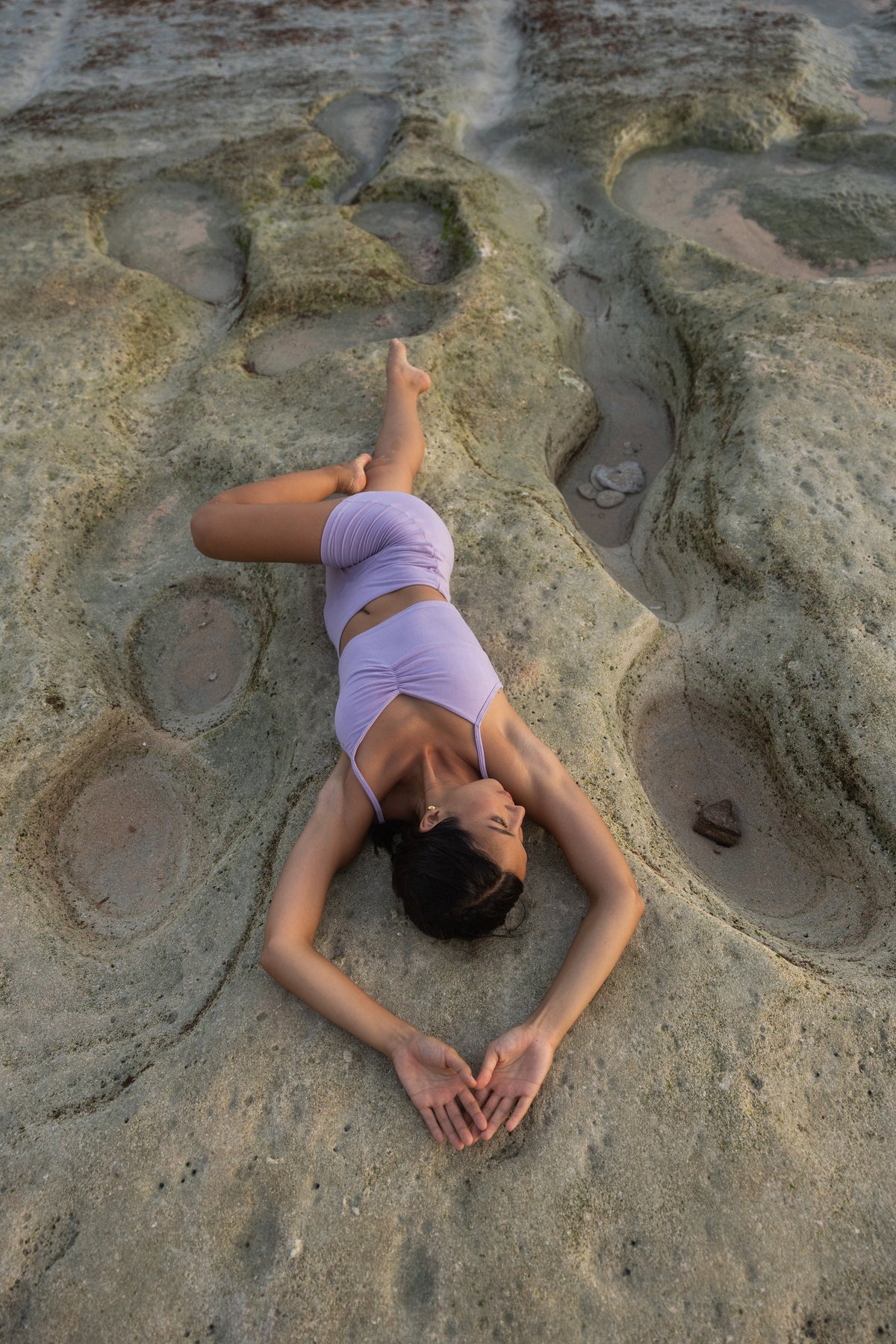 Woman lying on beach rocks in a backbend pose wearing an Adjustable Cotton Cami and matching shorts in Lilac #Color_Lilac